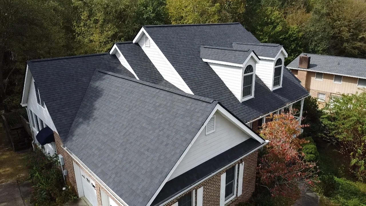 Aerial view of a new dark gray shingle roof with dormers on a brick and siding home